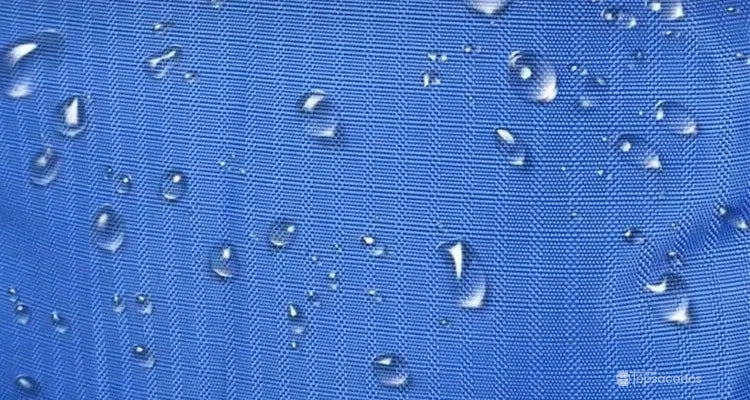 Sac à dos randonnée résistant à l’eau, gros plan sur le tissu bleu imperméable avec des gouttes de pluie visibles en surface.