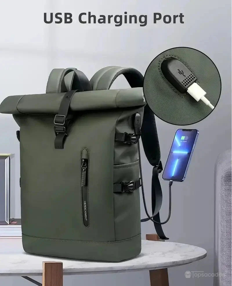 Sac a dos Roll Top vert avec port de chargement USB intégré sur le côté, posé sur une table ronde en intérieur, illustrant sa fonctionnalité moderne.