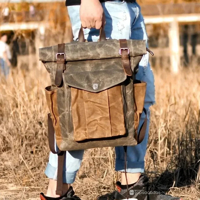 Sac à dos rolltop vintage homme porté à la main dans un champ sec, en situation réelle de marche