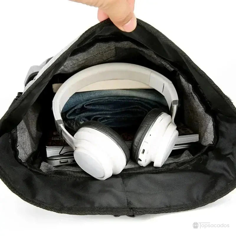 Sac à dos roulé vu de l’intérieur, contenant un casque audio blanc, des vêtements et des livres, illustrant sa grande capacité.