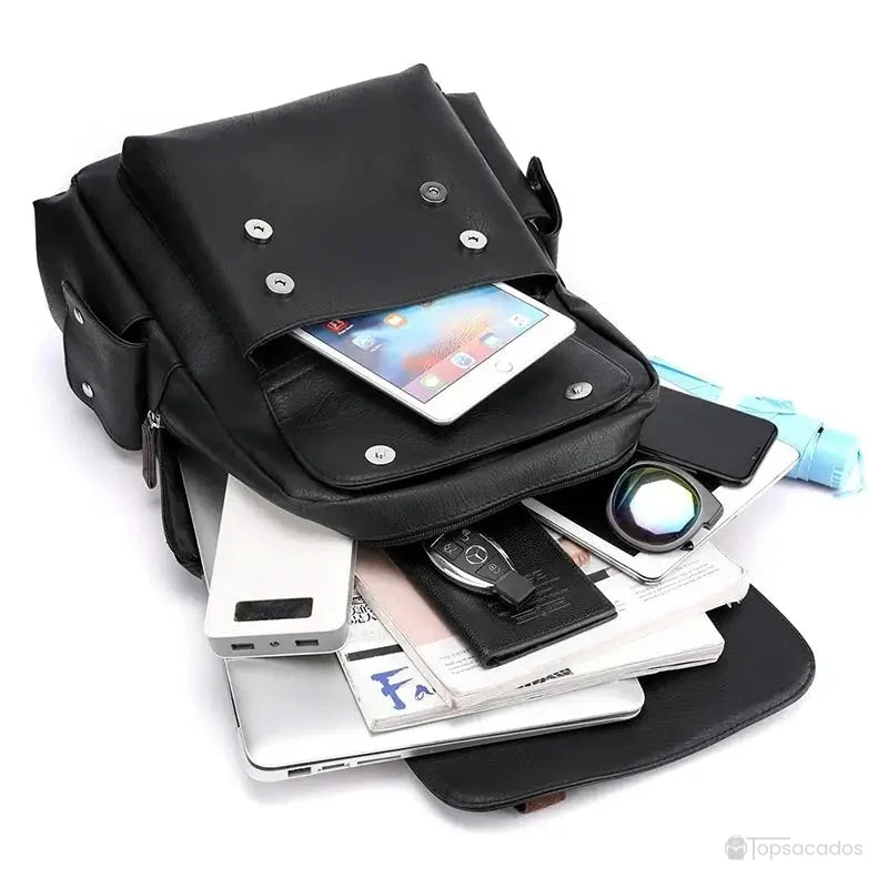 Sac à dos simili cuir noir ouvert, révélant son compartiment principal spacieux rempli de divers objets électroniques et de papeterie.