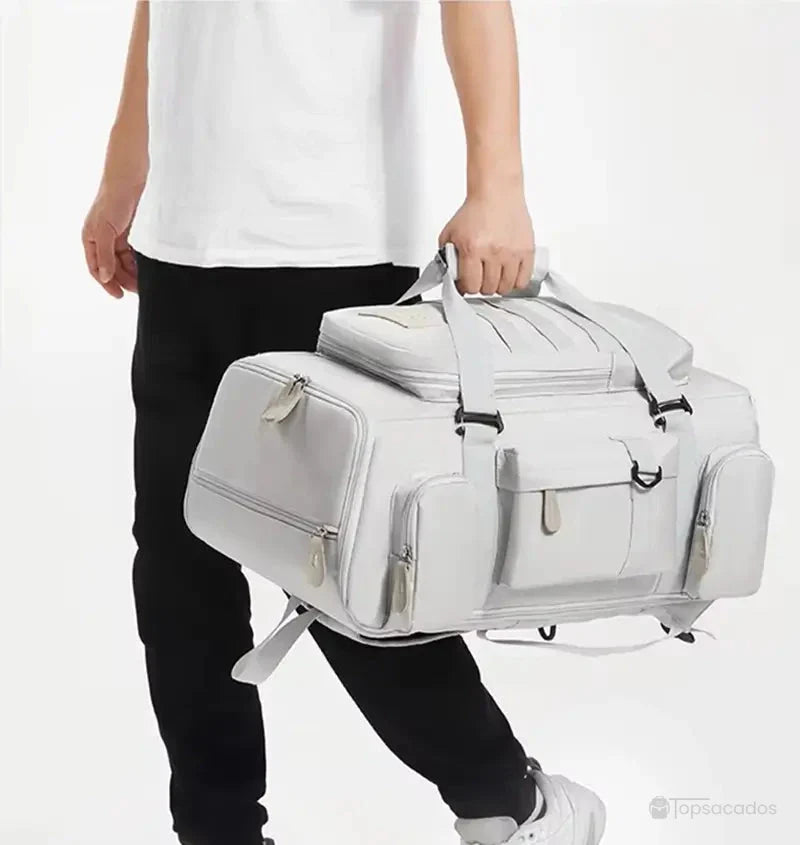 Sac à dos sport porté à la main par un homme, montrant sa fonction sac de voyage avec multiples poches zippées et design robuste.
