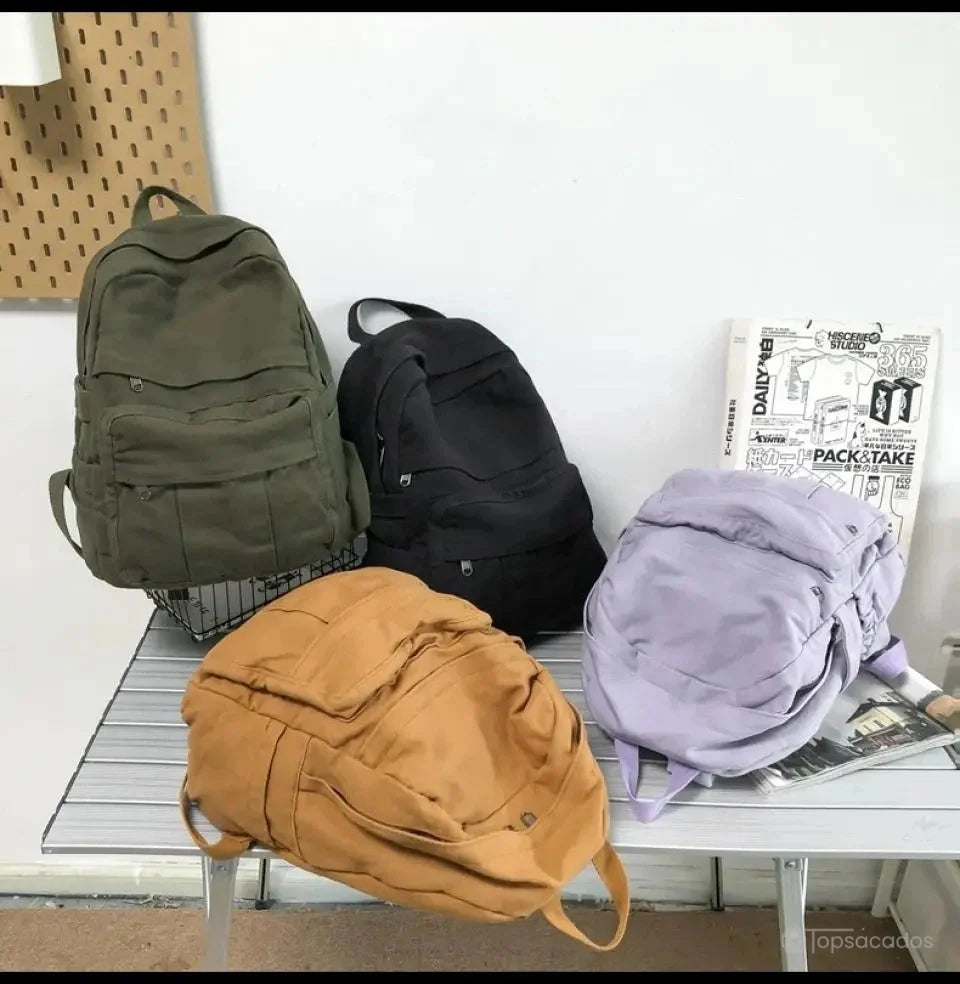Sac à dos toile décliné en quatre couleurs (vert, noir, marron et violet) exposé sur une table