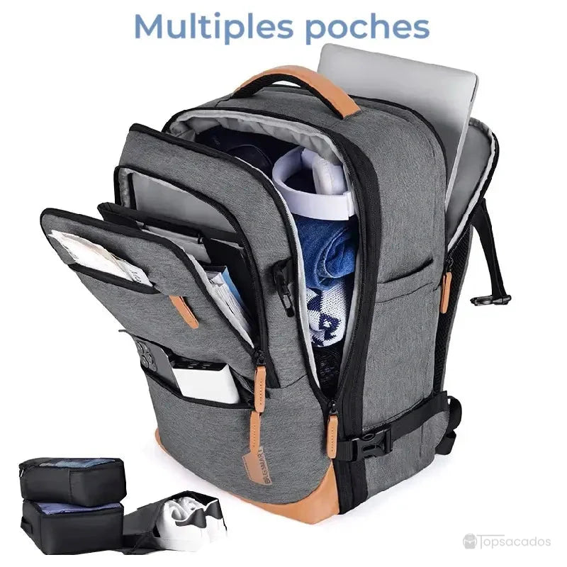 Sac à dos voyage extensible gris ouvert avec multiples poches remplies de vêtements, ordinateur portable et accessoires de voyage.
