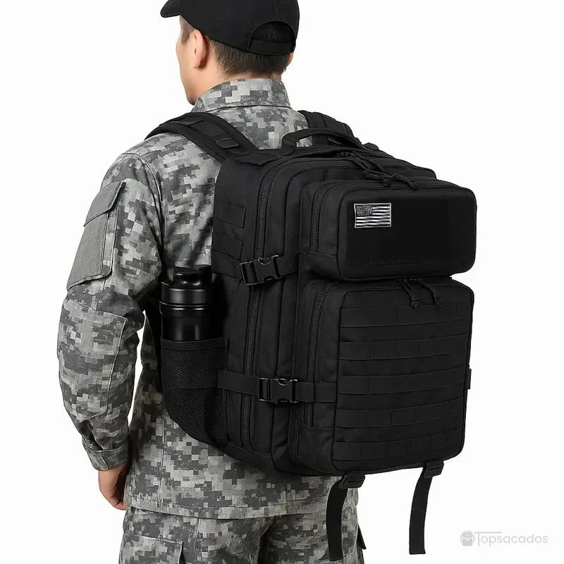 sac a dos militaire noir porté par une personne en tenue camouflage, vu de dos dans un environnement extérieur