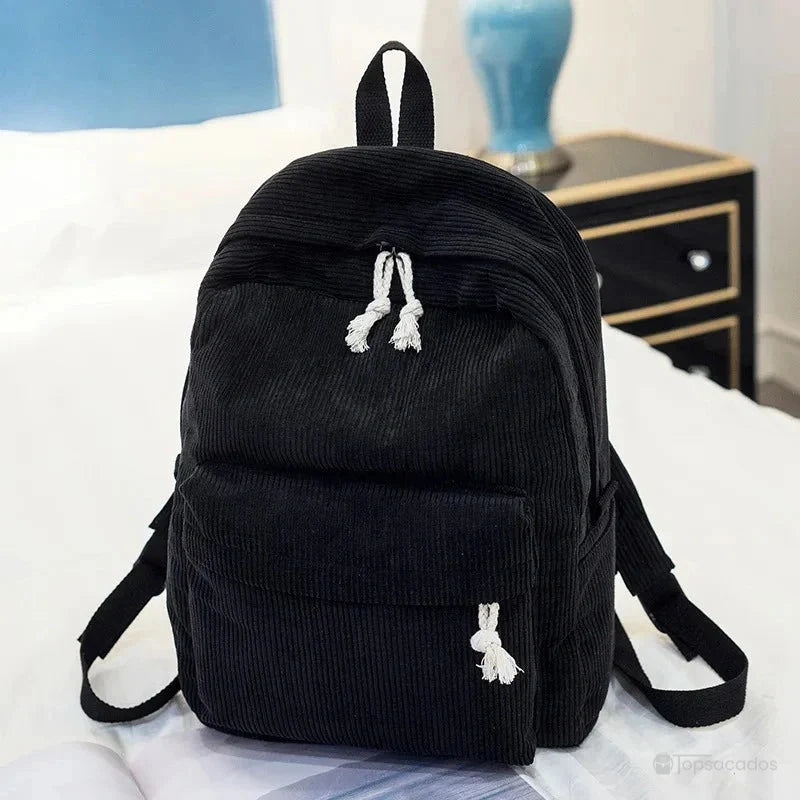sac à dos college en velours cotelé noir avec cordons blancs, placé sur un lit blanc avec lampe bleue en arrière-plan