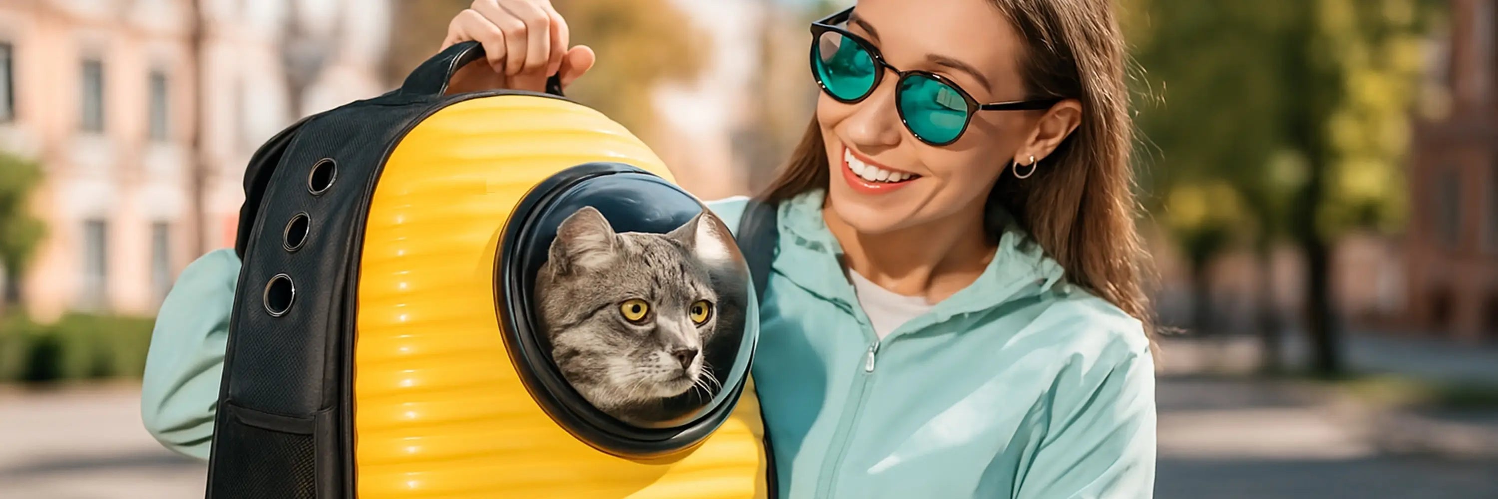 Femme souriante portant un sac à dos pour chat jaune avec un chat tigré à l'intérieur, en ville par une journée ensoleillée