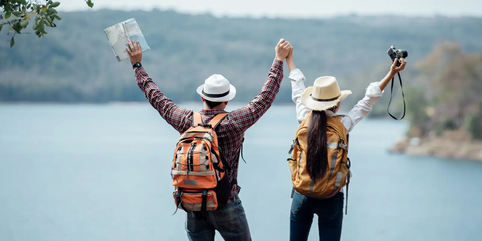 Couple de randonneurs face à un lac, levant les bras avec enthousiasme, chacun portant un sac à dos randonnée coloré