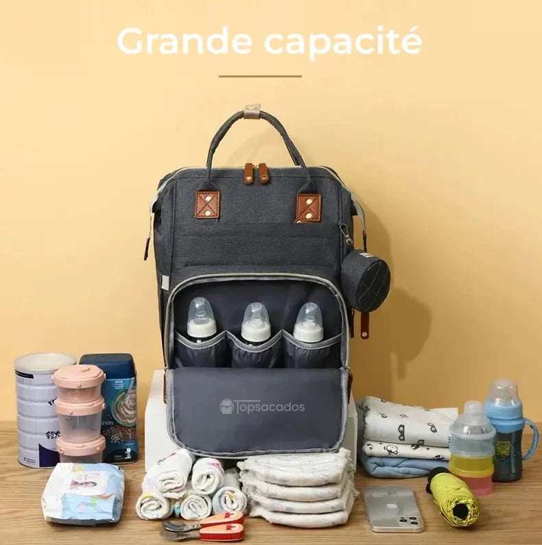 Sac à dos à langer avec port usb ouvert sur une table en bois, exposant son intérieur spacieux avec biberons, couches et accessoires pour bébé, sur fond jaune clair.