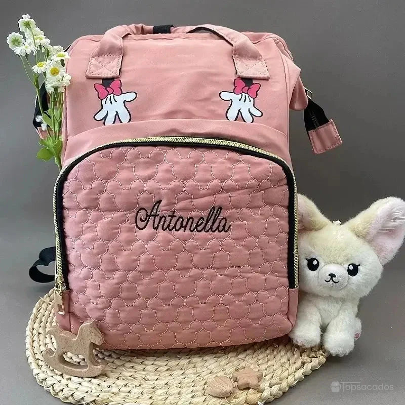 sac-a-dos-bebe-avec-son-prenom rose brodé Antonella, posé sur tapis tressé avec doudou lapin et fleurs, ambiance douce et enfantine