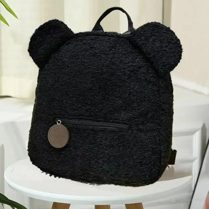 Sac a dos college Ourson noir en peluche avec oreilles d’ourson, posé sur un tabouret dans un intérieur lumineux