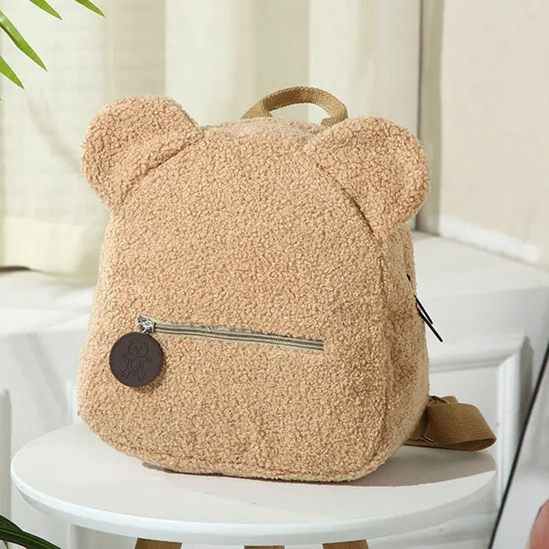 Sac a dos college Ourson beige clair avec oreilles ourson et fermeture zippée, posé sur tabouret en intérieur lumineux