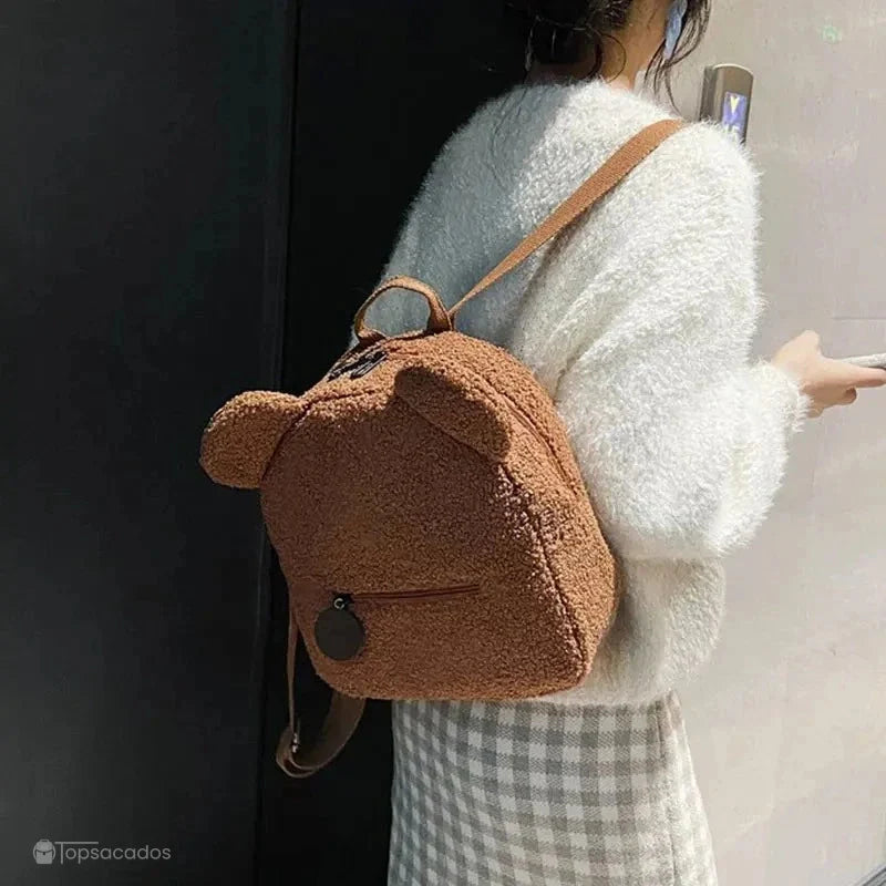 Sac a dos college Ourson marron porté sur l'épaule par une femme de dos, en tenue élégante dans un environnement lumineux