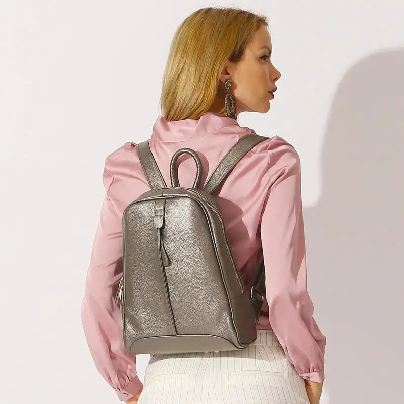 Sac à dos cuir femme tendance bronze porté par une femme vêtue d’une chemise rose, environnement en studio lumineux, ambiance mode urbaine.