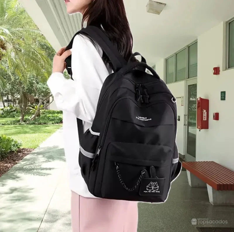 Sac à dos école noir porté par une jeune femme dans un campus universitaire avec arbres et bancs.