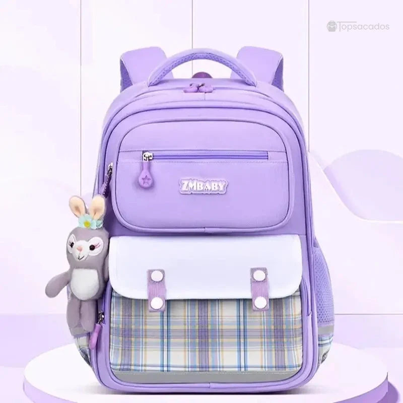 Sac à dos fille CP violet posé sur socle clair dans un décor pastel, avec peluche suspendue à la fermeture