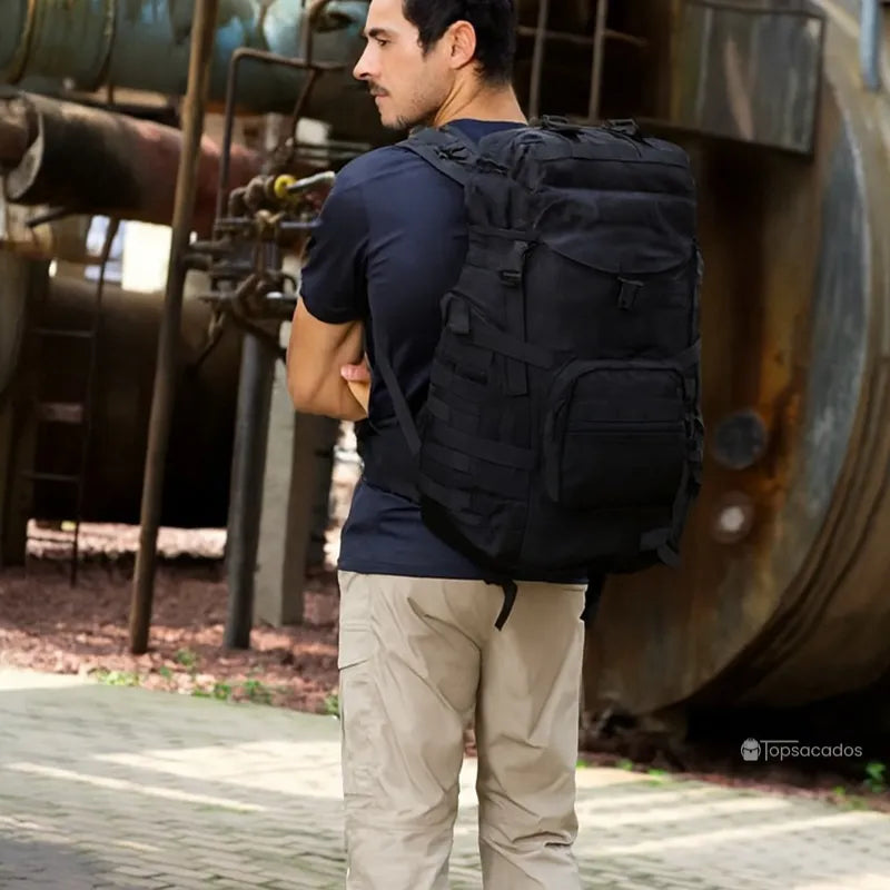 Sac à dos homme voyage noir porté par un homme barbu dans un environnement urbain industriel