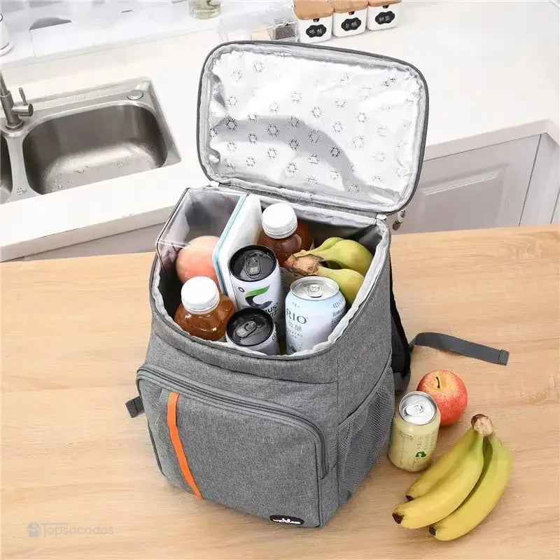 Sac à dos isotherme repas gris ouvert posé sur une table de cuisine, rempli de canettes, fruits, bouteilles et contenant isotherme, ambiance intérieure.