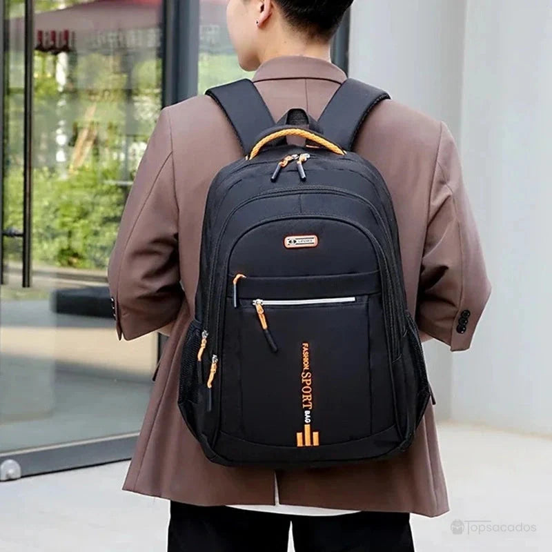 Sac a dos pour cours noir avec accents orange porté par un homme en veste marron clair dans un environnement urbain.