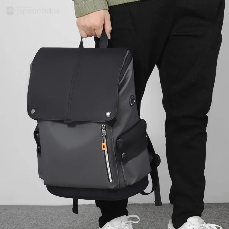 Sac à dos pour étudiant bicolore gris foncé et noir tenu à la main par un homme en tenue décontractée sur fond neutre.