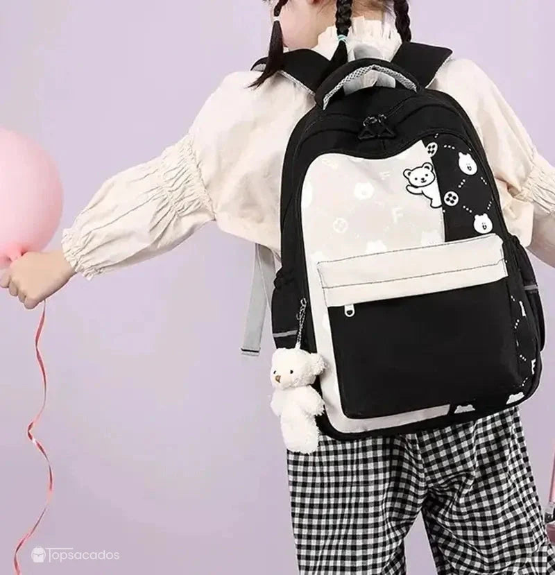 Sac à dos primaire fille noir porté par une jeune fille tenant un ballon rose, fond violet clair.