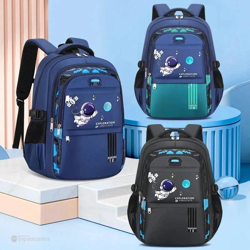 Sac à dos primaire garçon décliné en trois coloris : bleu, vert et noir, alignés sur fond pastel en perspective