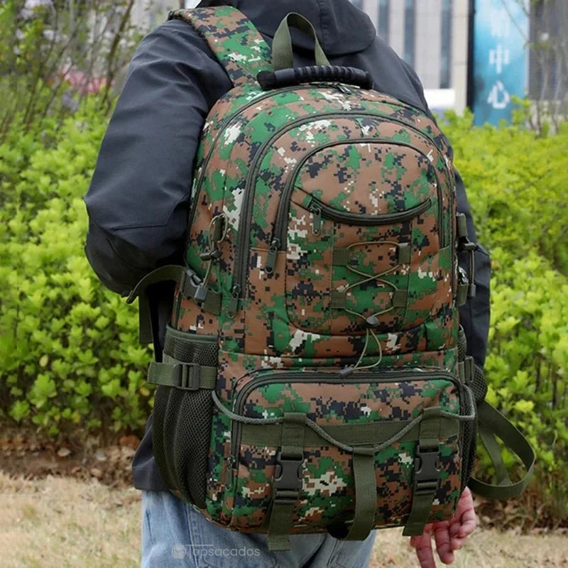 Sac à dos rando camouflage porté par un homme en veste noire, environnement urbain avec végétation