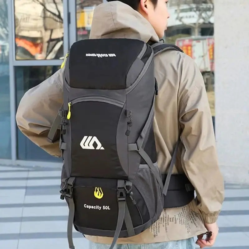 Sac à dos randonnée 50 litres noir porté par un randonneur en veste beige, devant un bâtiment vitré.