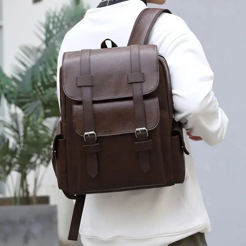 Sac à dos simili cuir marron foncé porté sur les épaules d’un homme vêtu d’un sweat blanc, photographié de dos.