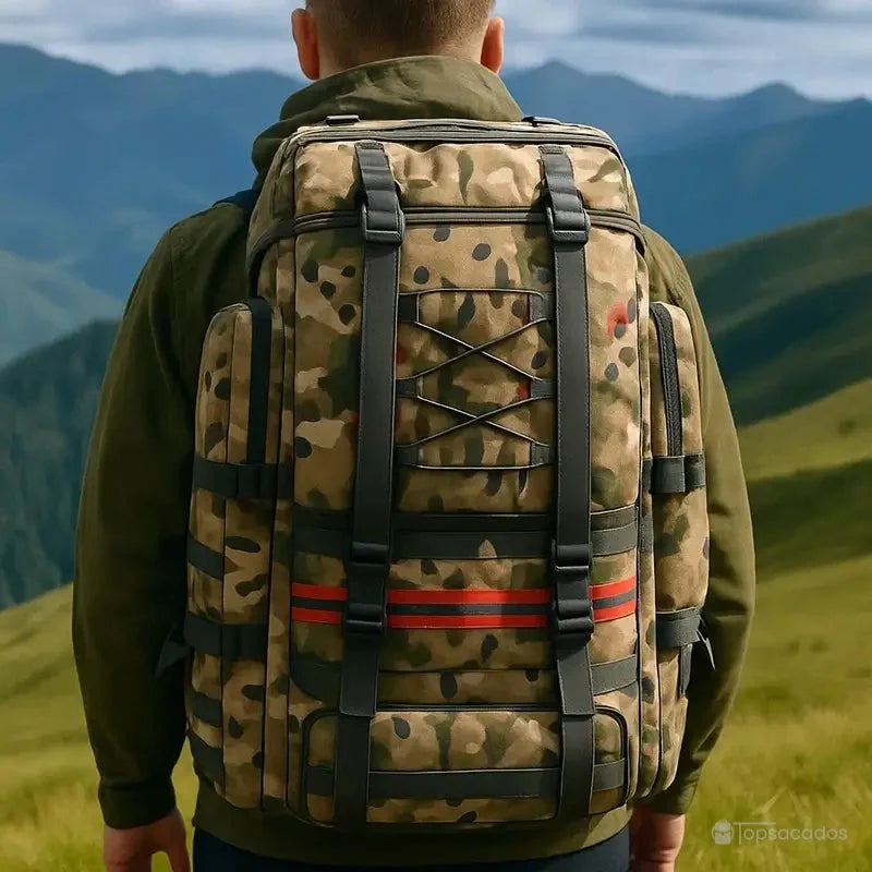 Sac à dos trekking camouflage porté en montagne par un homme en randonnée, vue sur fond de sommets verts.